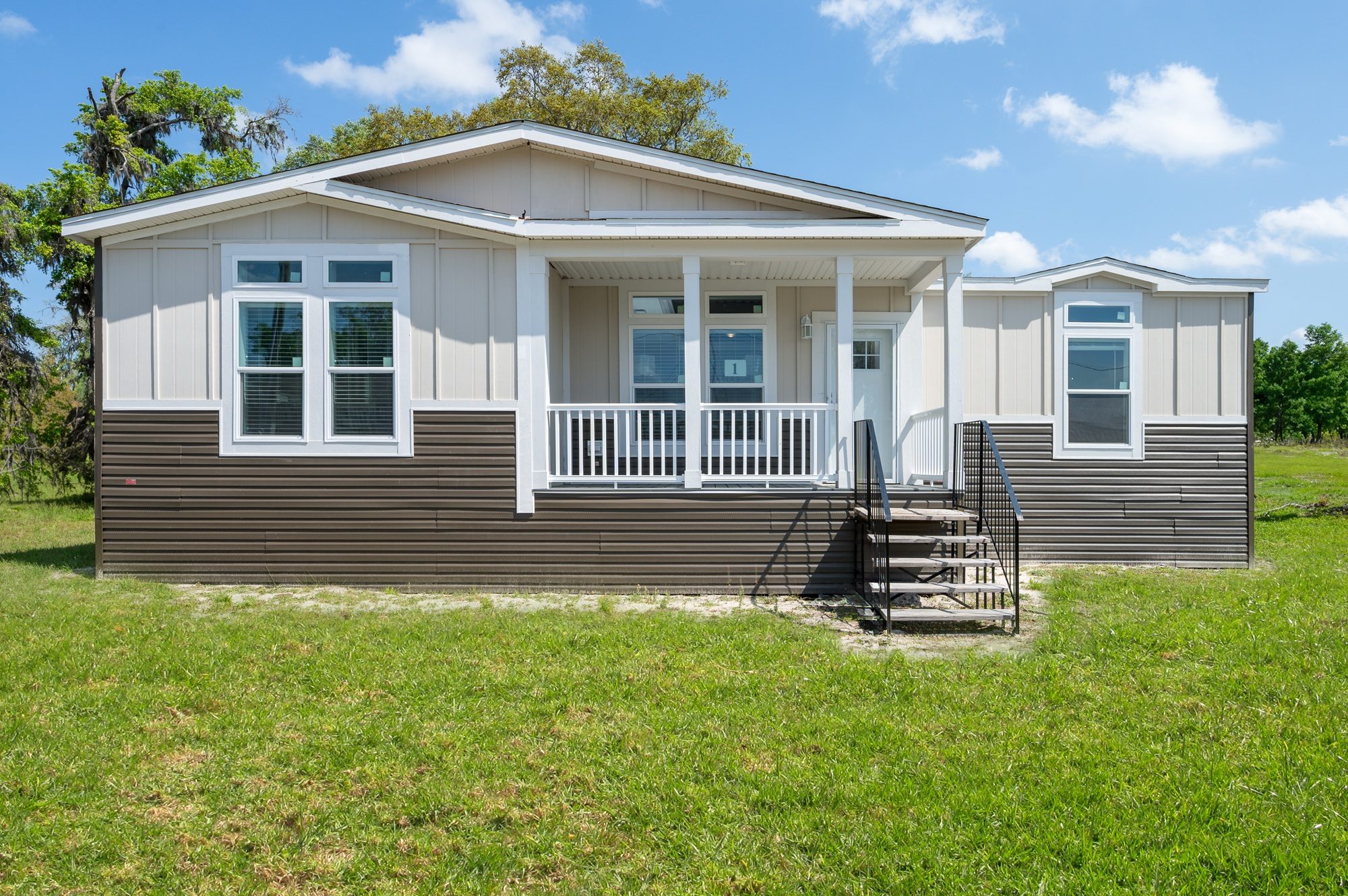 A manufactured home on the lot — board-and-batten gable, a covered front porch and a full-width entry deck.